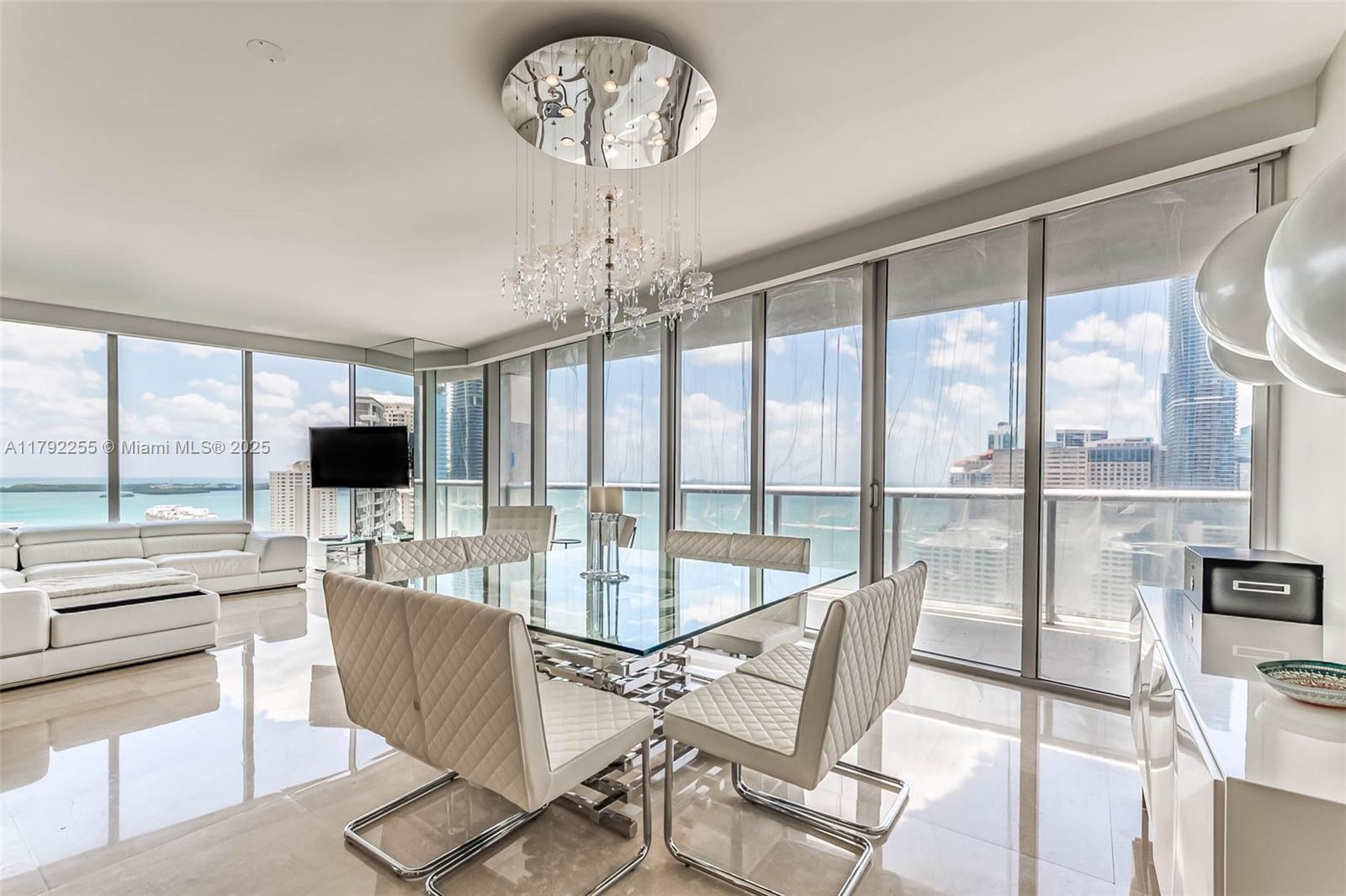 A modern dining area features a glass table, quilted chairs, and floor-to-ceiling windows overlooking water — 495 Brickell Ave # 2801, Miami FL 33131, MIAMI, FL