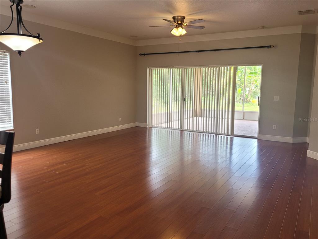 An empty living room features hardwood floors, a ceiling fan, and sliding glass patio doors — 20722 GREAT LAUREL AVENUE, TAMPA, FL