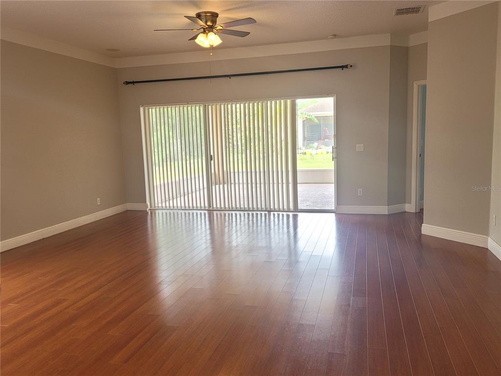 An empty living room features hardwood floors, a ceiling fan, and sliding glass patio doors — 20722 GREAT LAUREL AVENUE, TAMPA, FL