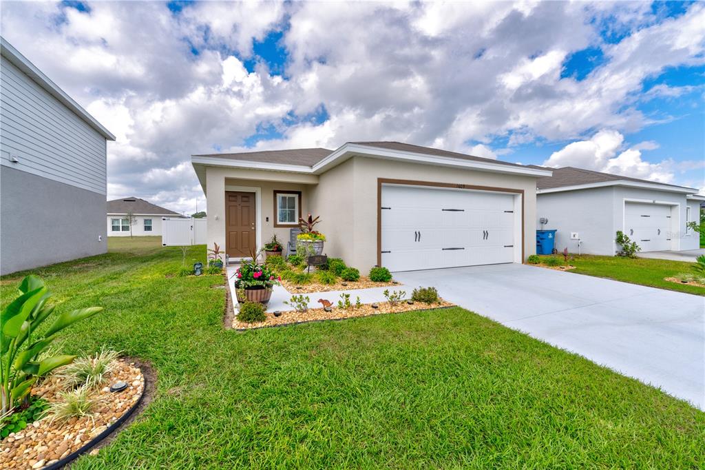 A single-story house with a white garage, tan exterior, and a landscaped front yard — 1609 FINNIGAN CIRCLE, HAINES CITY, FL