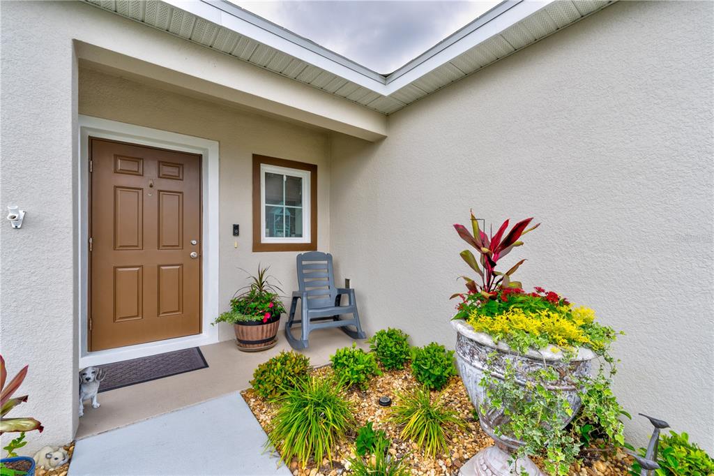 A front entryway features a brown door, a rocking chair, and a large potted plant — 1609 FINNIGAN CIRCLE, HAINES CITY, FL
