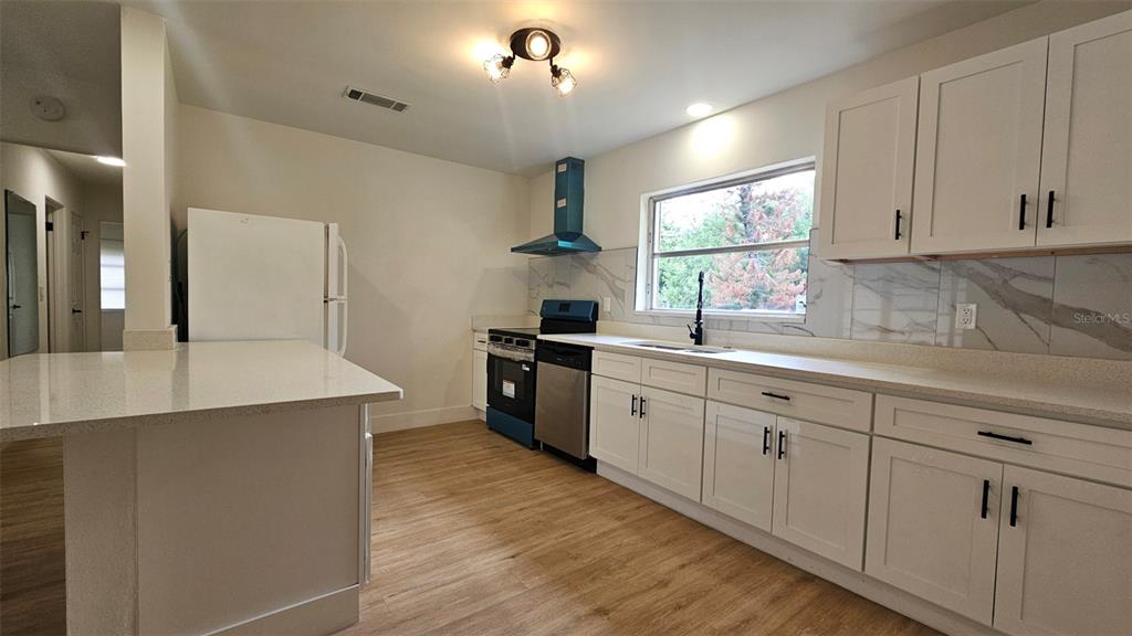 A kitchen features white cabinets, a quartz countertop, stainless steel appliances, and wood-look flooring — 924 FERN AVENUE, COCOA, FL