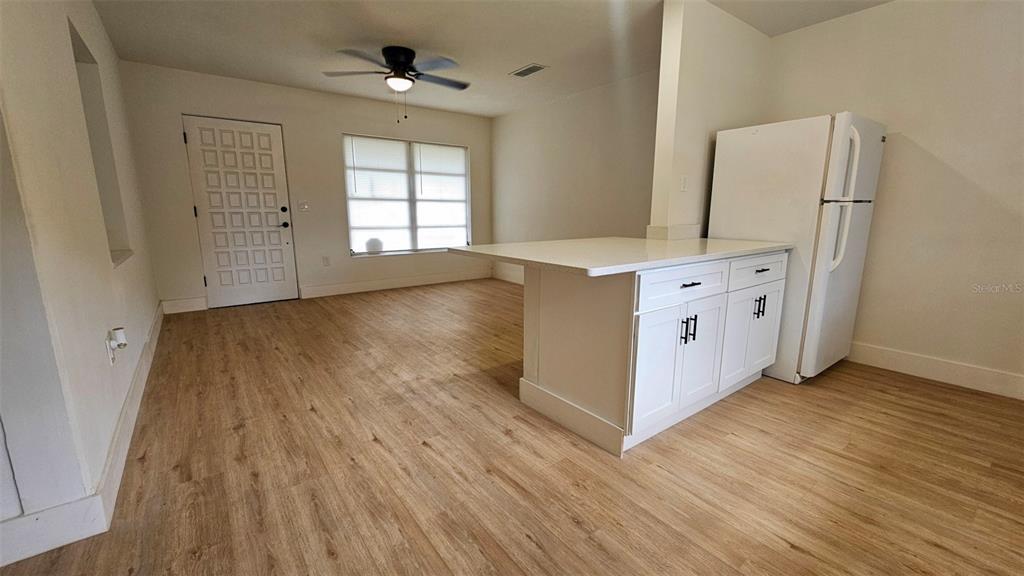 A kitchen with a white island and refrigerator opens into a living area with wood-look flooring — 924 FERN AVENUE, COCOA, FL