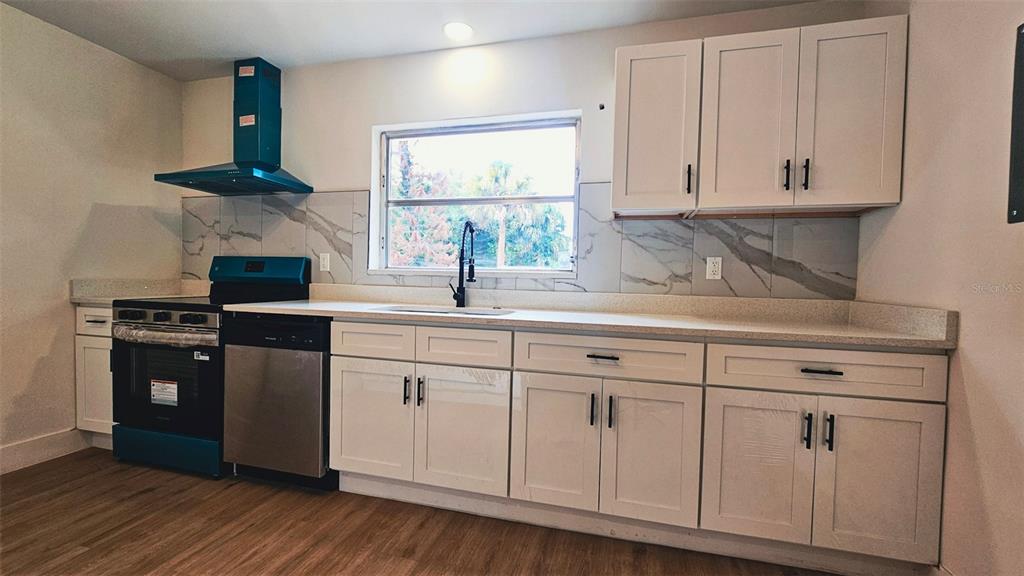 A kitchen features white cabinets, a black range, a window, and marble-patterned backsplash tiles — 924 FERN AVENUE, COCOA, FL