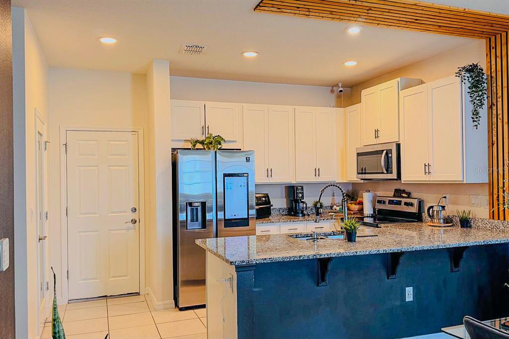 A kitchen features white cabinetry, granite countertops, a stainless steel refrigerator, and a breakfast bar — 1776 FULFILLMENT DRIVE, KISSIMMEE, FL