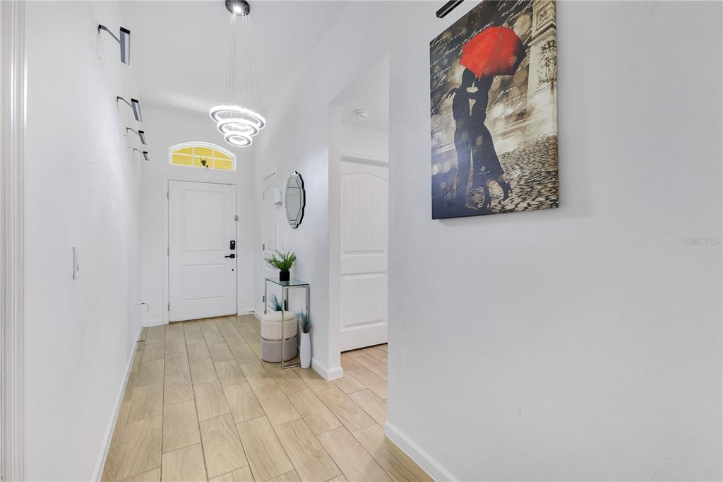 A bright entryway features light wood-look tile flooring, a modern chandelier, and white walls — 723 ROBIN COURT, KISSIMMEE, FL