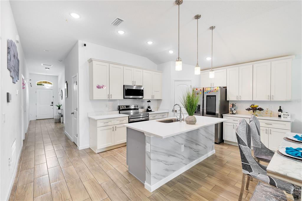 A modern kitchen features white cabinetry, a marble-patterned island, and light wood-look tile flooring — 723 ROBIN COURT, KISSIMMEE, FL
