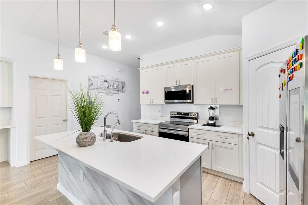 A modern kitchen features white cabinetry, a marble-patterned island with a sink, and pendant lighting — 723 ROBIN COURT, KISSIMMEE, FL