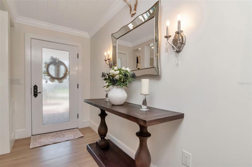 A foyer features a wooden console table, a decorative mirror, and wall sconces — 4927 W MELROSE AVENUE N, TAMPA, FL