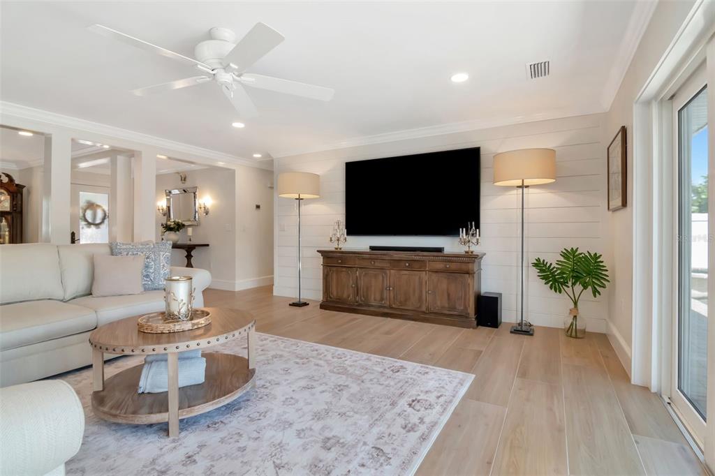 A living room features a shiplap wall, a large television, and light wood flooring — 4927 W MELROSE AVENUE N, TAMPA, FL