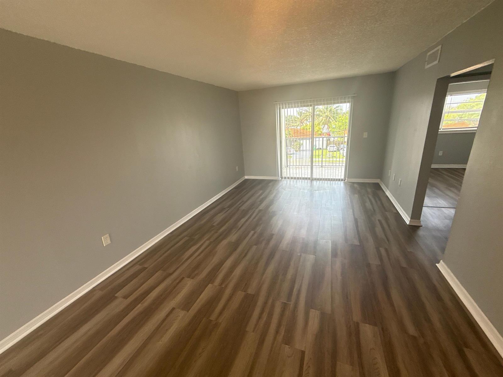 An empty living room features gray walls, wood-look flooring, and a sliding glass balcony door — 2605 NW 135th Street # 309, Opa-Locka FL 33167, OPA-LOCKA, FL