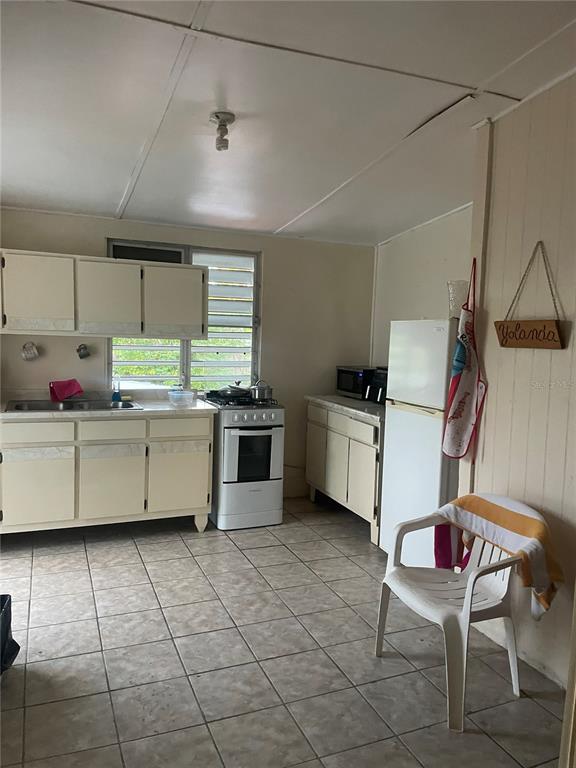 A kitchen features off-white cabinets, a white stove, a refrigerator, and tiled flooring — Lot 3 CALLE 3, GUANICA, PR