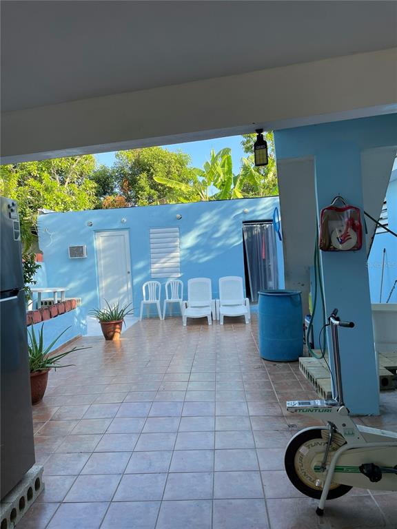 A tiled outdoor patio features four white chairs, a blue barrel, and an exercise bike — Lot 3 CALLE 3, GUANICA, PR