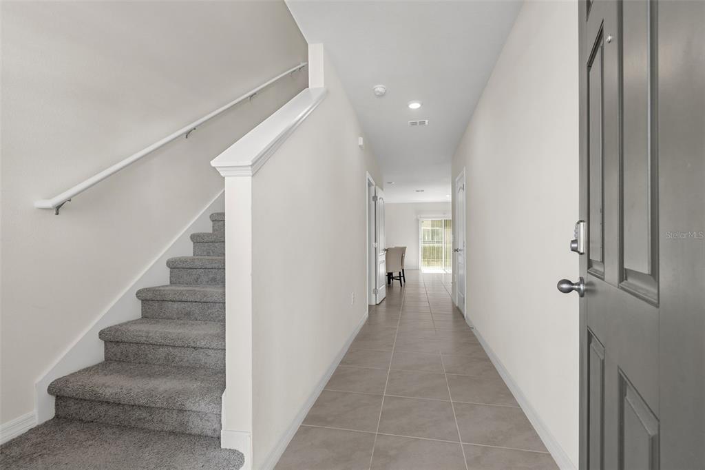 An entryway features gray tile flooring, a carpeted staircase with a white railing, and white walls — 2722 PUFFIN PLACE, DAVENPORT, FL