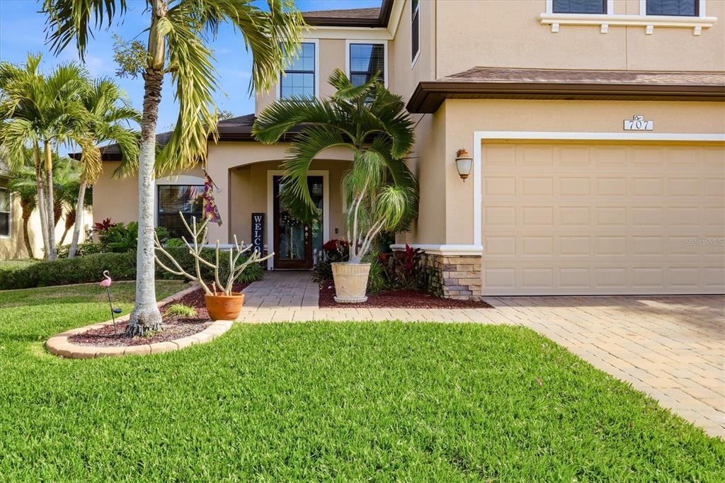 A two-story house exterior features a beige stucco facade, a paved driveway, and palm trees — 707 DOGWOOD RUN, BRADENTON, FL