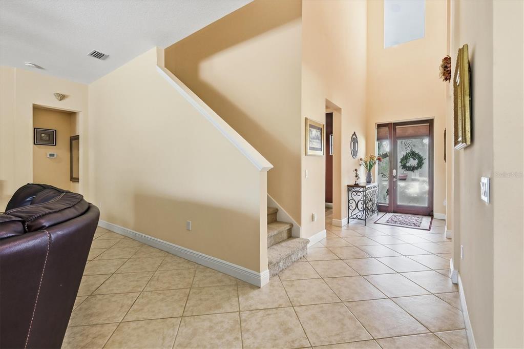 An entryway features a high ceiling, tiled floor, carpeted stairs, and a glass-paneled front door — 707 DOGWOOD RUN, BRADENTON, FL