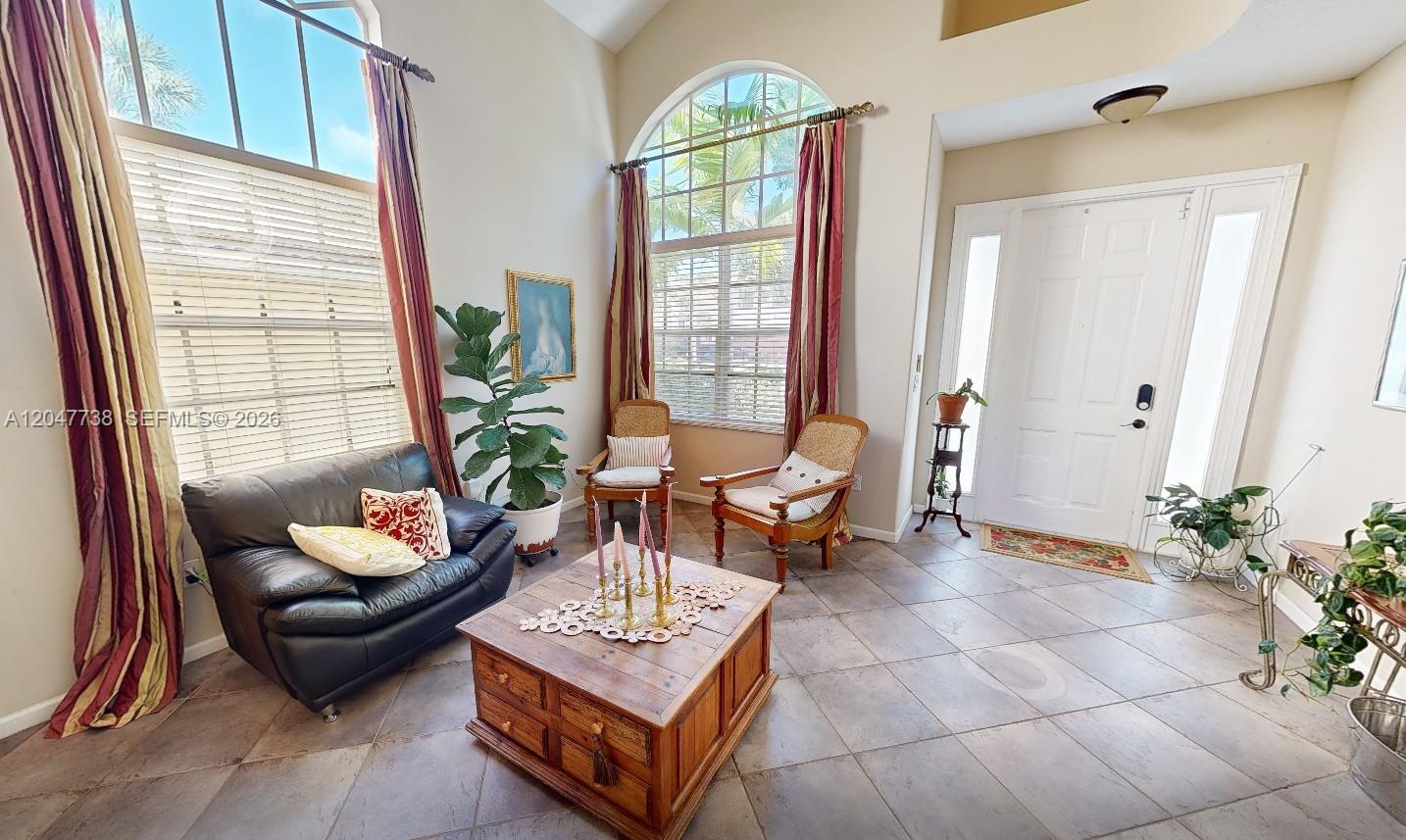 A living room features high ceilings, large arched windows, tile flooring, and a wooden coffee table — 9640 Wyeth Ct, Wellington FL 33414, WELLINGTON, FL