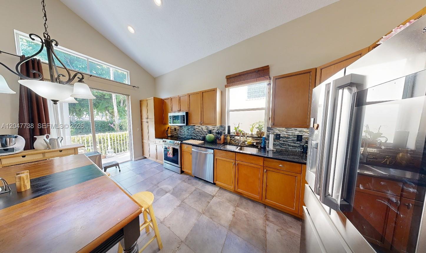 A kitchen features wooden cabinets, dark granite countertops, stainless steel appliances, and a vaulted ceiling — 9640 Wyeth Ct, Wellington FL 33414, WELLINGTON, FL