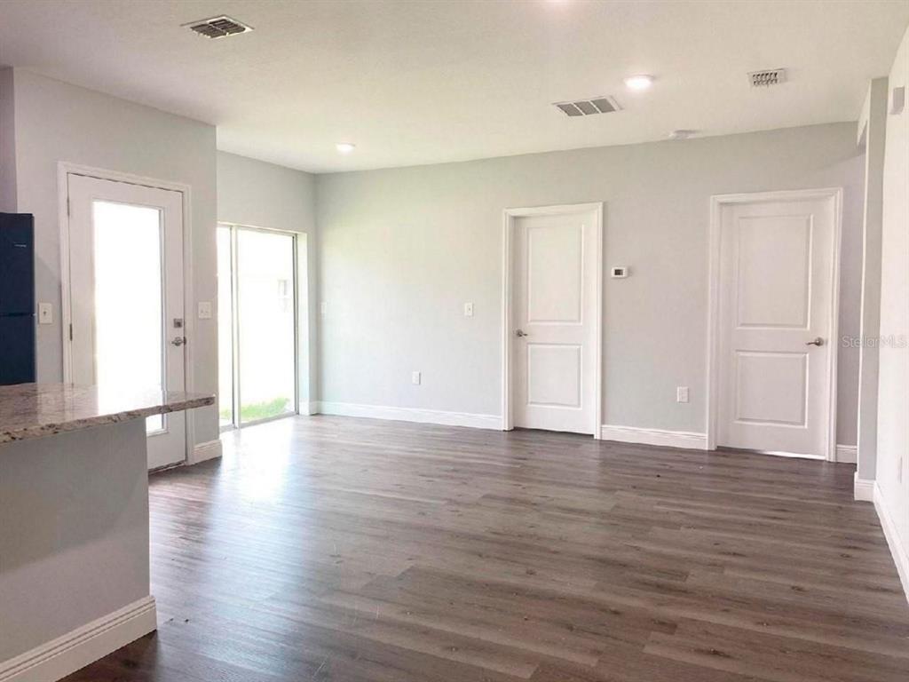 An empty room features light gray walls, wood-look flooring, two white doors, and a glass door — 2115 PUFFIN STREET UNIT 2117, SEBRING, FL