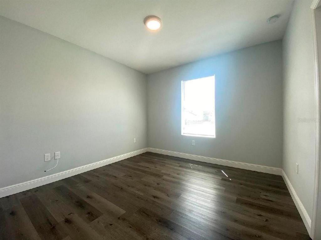 An empty bedroom features light gray walls, white trim, and dark wood-look flooring — 2115 PUFFIN STREET UNIT 2117, SEBRING, FL
