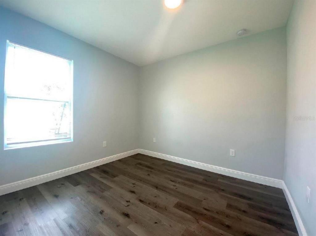An empty bedroom features light gray walls, white trim, and dark wood-look flooring — 2115 PUFFIN STREET UNIT 2117, SEBRING, FL