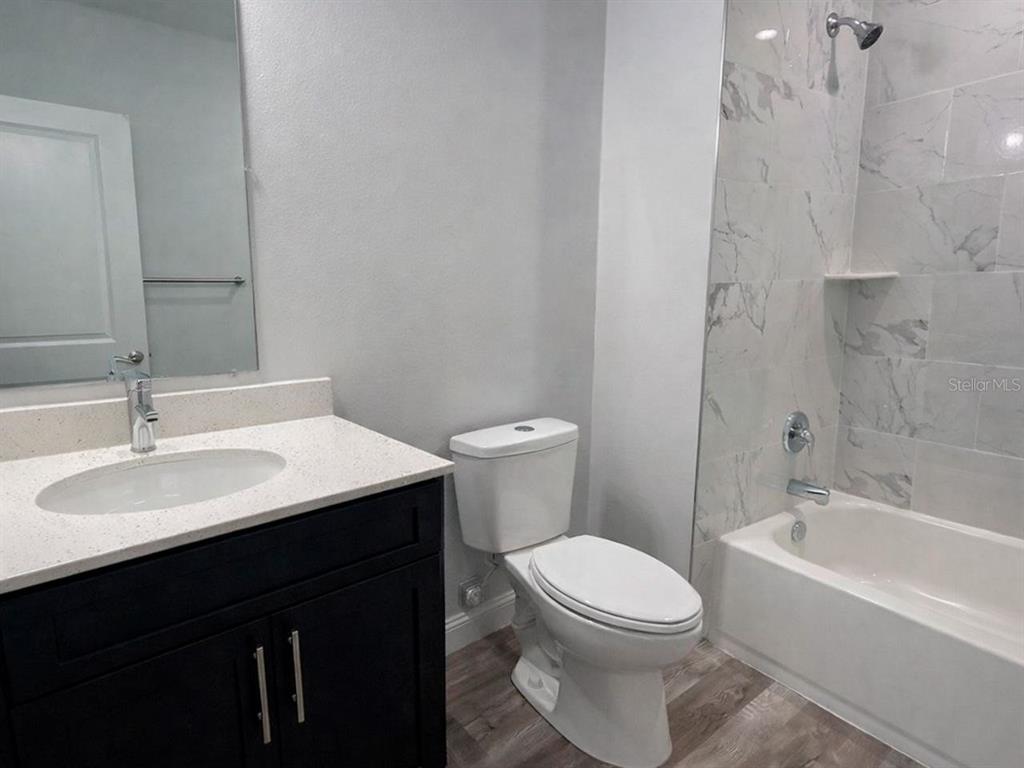 A bathroom features a dark vanity, white countertop, toilet, and a tiled shower-tub combination — 2115 PUFFIN STREET UNIT 2117, SEBRING, FL