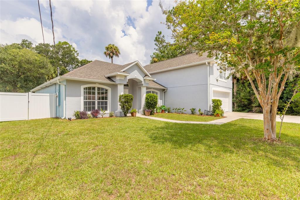 A light gray single-story house with a white fence and a large tree in front — 28 PILLORY LANE, PALM COAST, FL