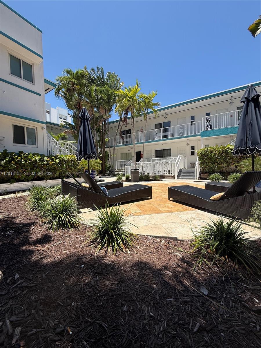A courtyard features lounge chairs, umbrellas, and tropical landscaping between two-story apartment buildings — 7710 Harding Ave # 7, Miami Beach FL 33141, MIAMI BEACH, FL
