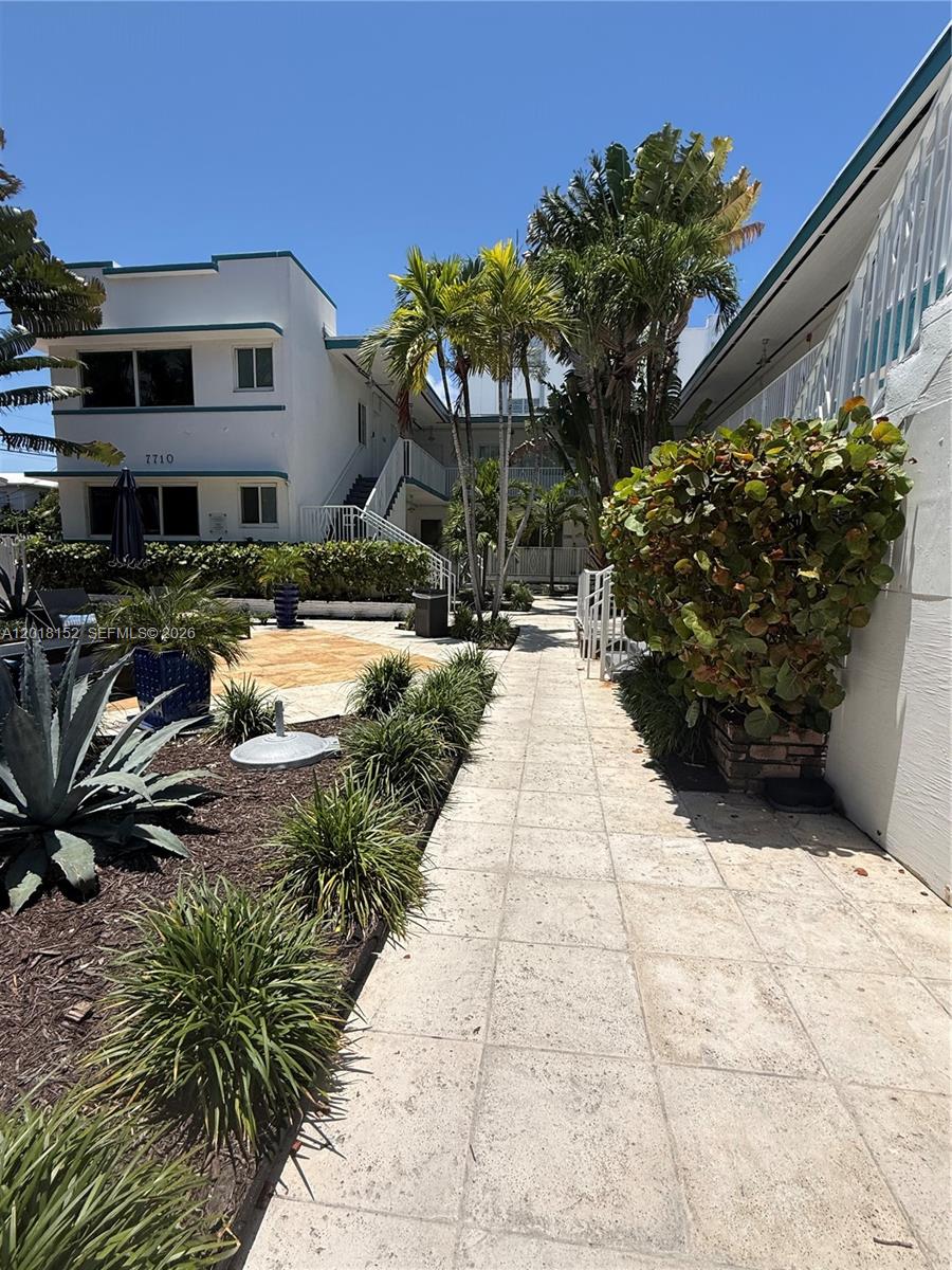 A paved walkway leads through a landscaped courtyard toward a two-story white apartment building — 7710 Harding Ave # 7, Miami Beach FL 33141, MIAMI BEACH, FL