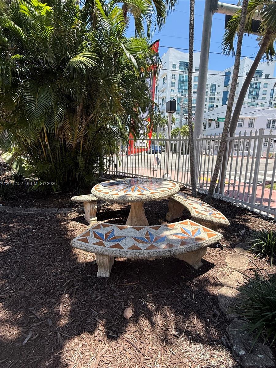 A mosaic-tiled stone table and curved benches sit in a mulched area near a fence — 7710 Harding Ave # 7, Miami Beach FL 33141, MIAMI BEACH, FL
