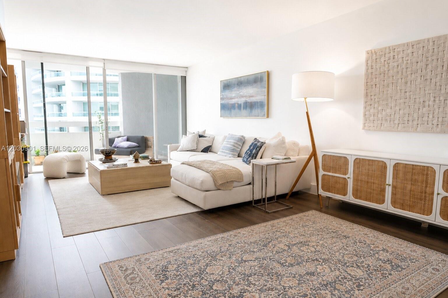 A bright living room features a white sectional sofa, wooden coffee table, and floor lamp — 1627 Brickell Ave # 1005, Miami FL 33129, MIAMI, FL