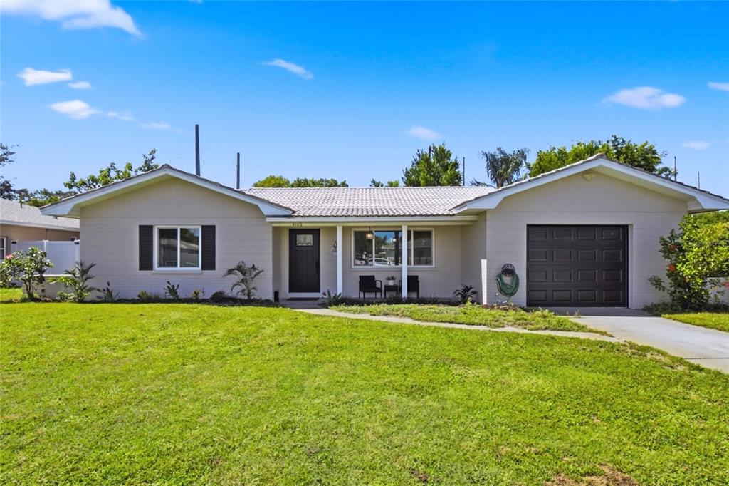 A single-story house with a light-colored brick exterior, dark garage door, and a front lawn — 4100 18TH AVENUE N, ST PETERSBURG, FL