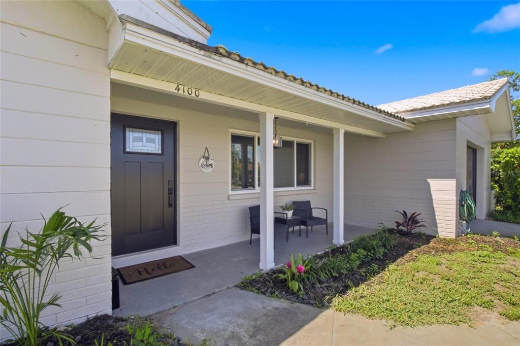 A covered front porch features a dark door, two chairs, and a small garden bed — 4100 18TH AVENUE N, ST PETERSBURG, FL