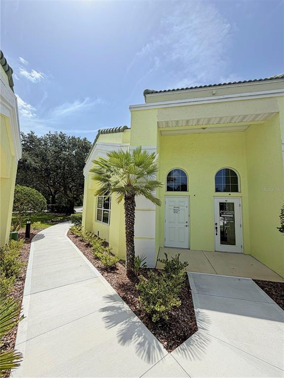 A yellow commercial building exterior features two white doors and a palm tree — 50 CYPRESS POINT PARKWAY UNIT B4, PALM COAST, FL