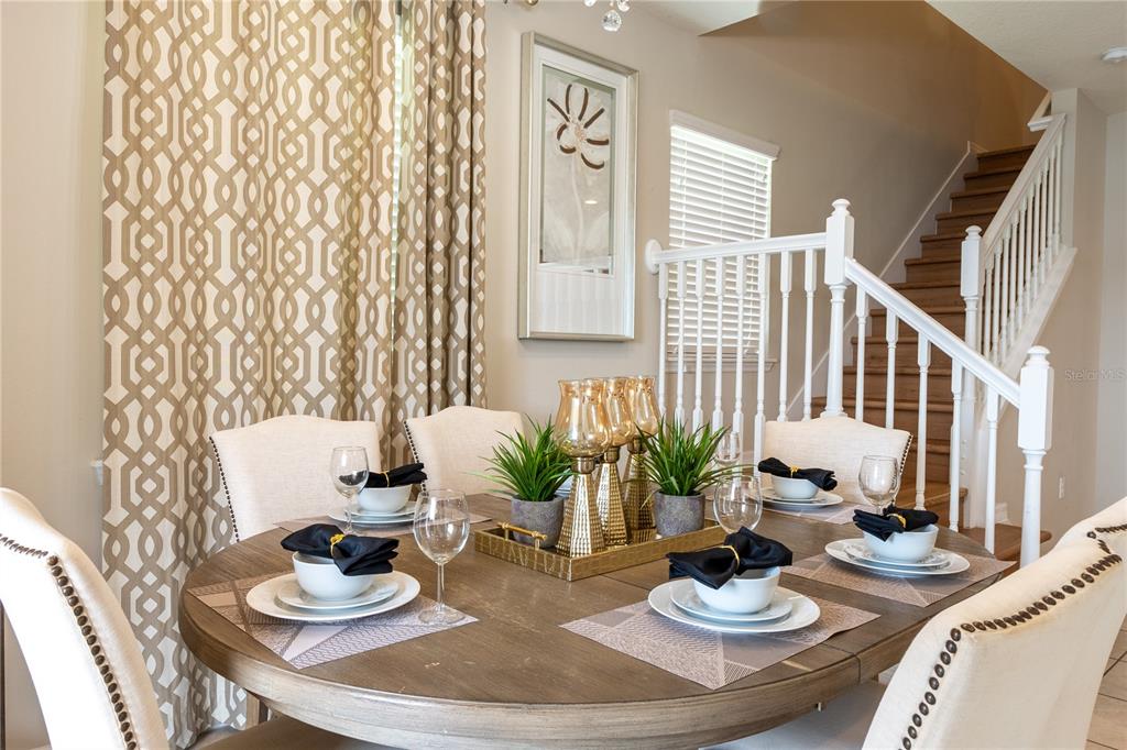A round wooden dining table with place settings sits in a room with patterned curtains — 8894 GENEVE COURT, KISSIMMEE, FL