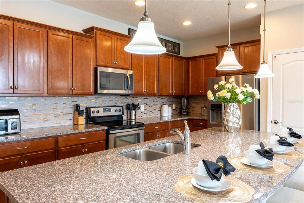 A kitchen features wooden cabinets, granite countertops, a central island, and stainless steel appliances — 8894 GENEVE COURT, KISSIMMEE, FL
