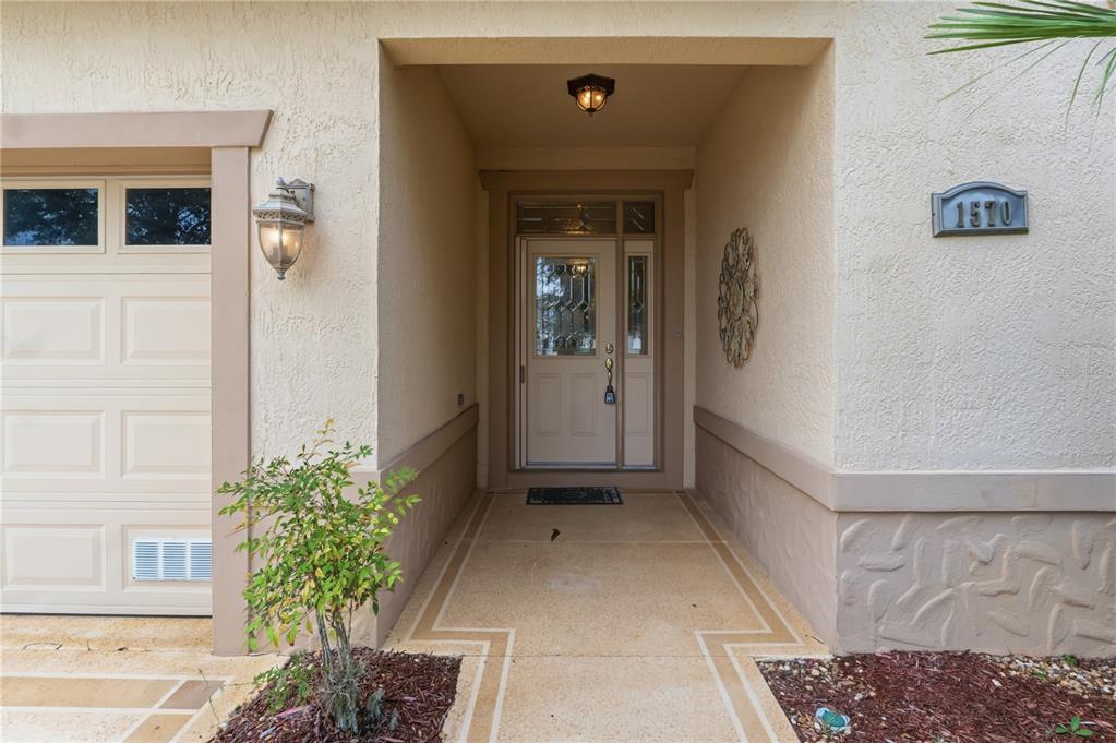 A beige stucco house exterior features a covered entryway with a decorative front door — 1570 GIFFORD COURT, THE VILLAGES, FL