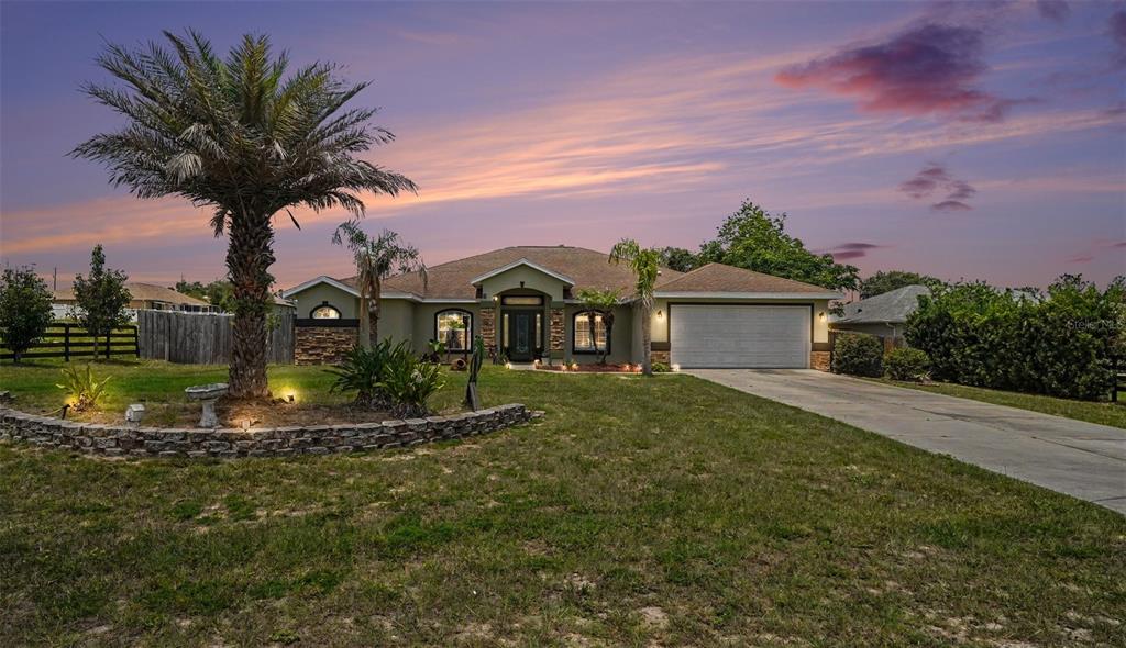 A single-story house with a palm tree, stone landscaping, and a concrete driveway at dusk — 10300 SW 47TH AVENUE, OCALA, FL