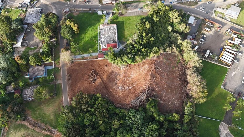 An aerial view shows a cleared dirt lot surrounded by trees, buildings, and a parking area — BO MIRAFLORES PARC. 2, ARECIBO, PR