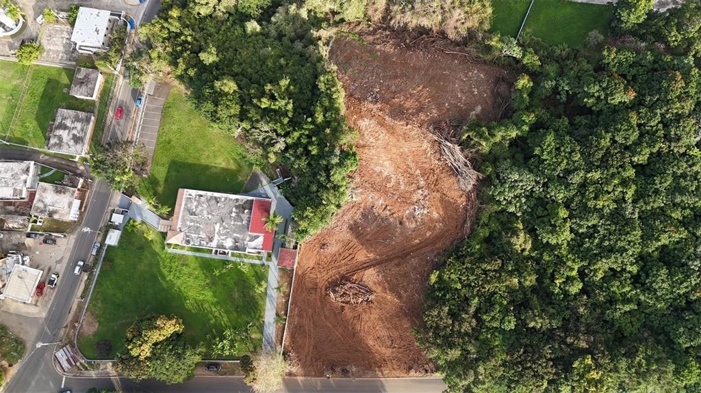 An aerial view shows a cleared dirt lot adjacent to a house and dense forest — BO MIRAFLORES PARC. 2, ARECIBO, PR