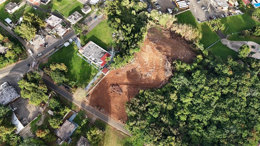 An aerial view shows a cleared, dirt-covered lot surrounded by trees and residential buildings — BO MIRAFLORES PARC. 2, ARECIBO, PR