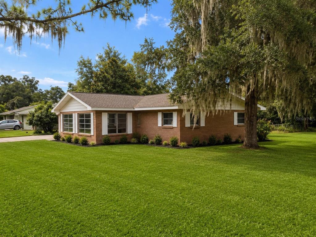 A single-story brick house with a white-trimmed roof sits on a large, grassy lawn — 13895 SE 100TH AVENUE, SUMMERFIELD, FL