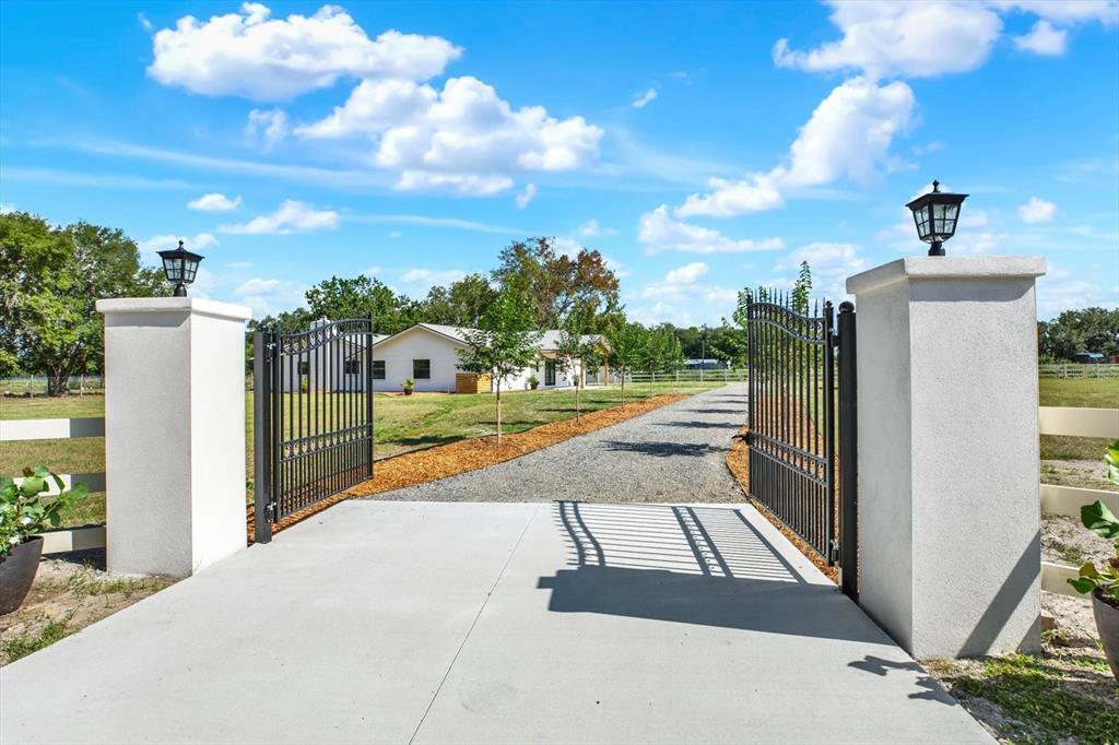 A gravel driveway leads to a white house through an open black metal gate — 2515 RAGINS LANE, PLANT CITY, FL