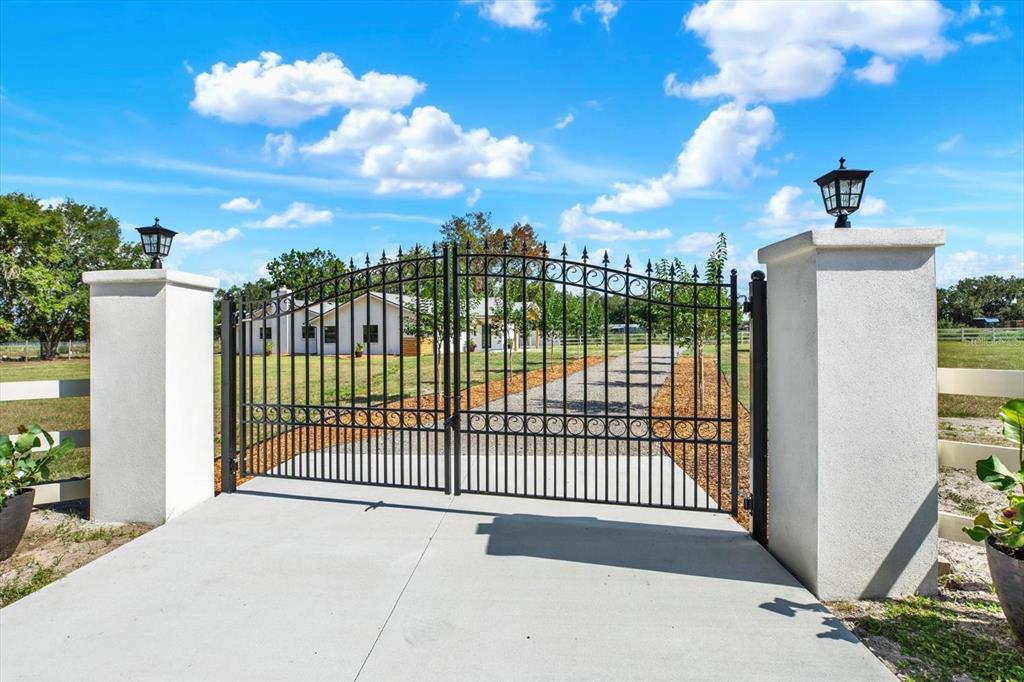 A black metal gate stands between two concrete pillars leading to a house and driveway — 2515 RAGINS LANE, PLANT CITY, FL