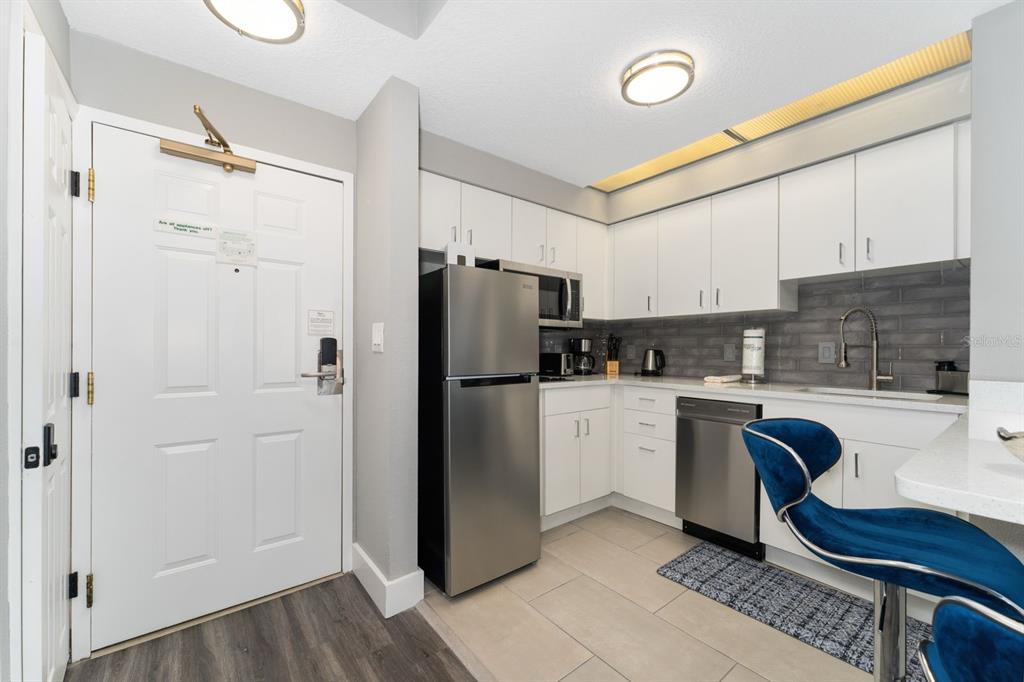 A small kitchen features white cabinets, stainless steel appliances, and a blue velvet bar stool — 7601 CANADA AVENUE UNIT 617, ORLANDO, FL