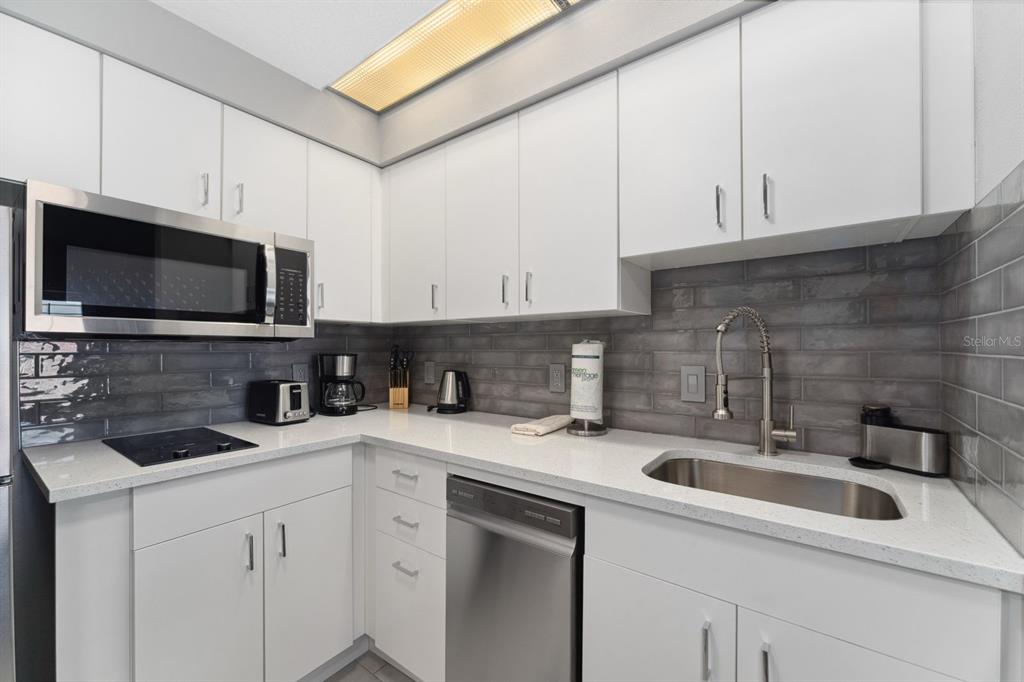 A modern kitchen features white cabinets, quartz countertops, a stainless steel dishwasher, and gray backsplash — 7601 CANADA AVENUE UNIT 617, ORLANDO, FL