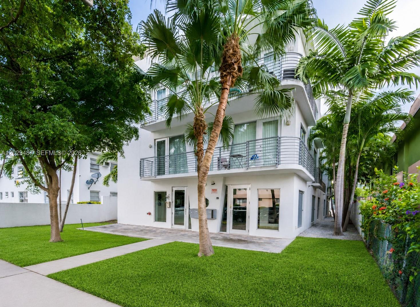 A three-story white apartment building with balconies and palm trees sits on a grassy lawn — 945 Michigan Ave # 5, Miami Beach FL 33139, MIAMI BEACH, FL