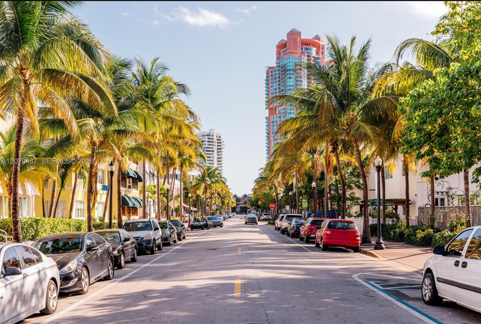 A street lined with palm trees and parked cars leads toward a tall pink building — 945 Michigan Ave # 5, Miami Beach FL 33139, MIAMI BEACH, FL