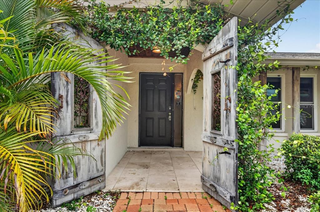 A front entryway features a dark door framed by weathered wooden shutters and lush greenery — 1221 E LIME STREET, TARPON SPRINGS, FL