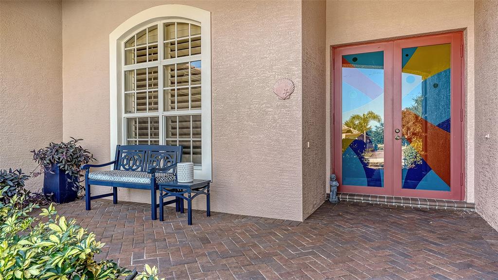A front porch features a blue bench, a window with shutters, and double glass doors — 7522 CONSERVATION COURT, SARASOTA, FL